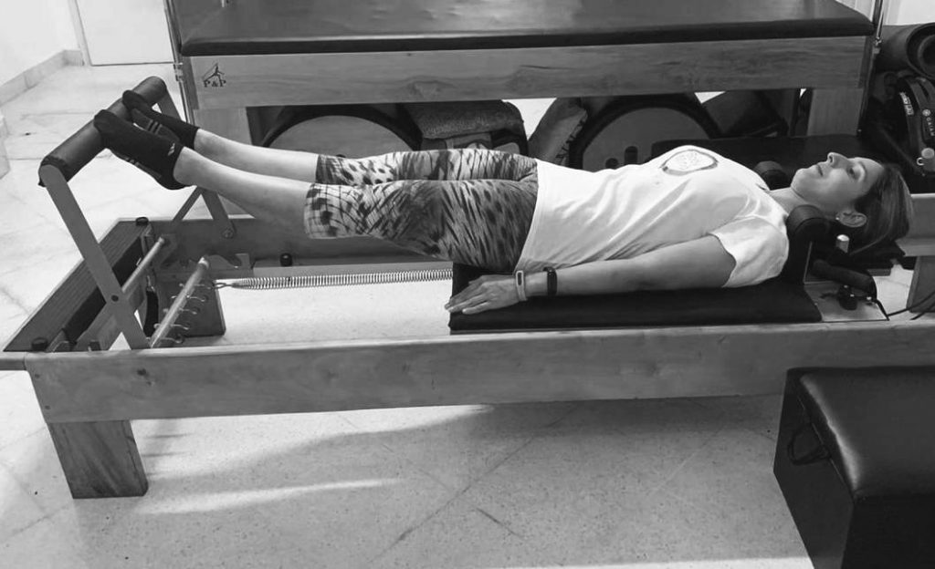 mujer realizando ejercicio de pilates reformer conocido como footwork series