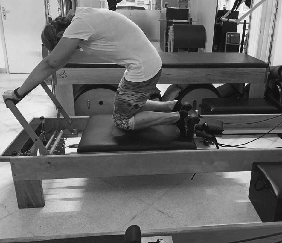 mujer realizando ejercicio de pilates reformer conocido como knee stretch round back