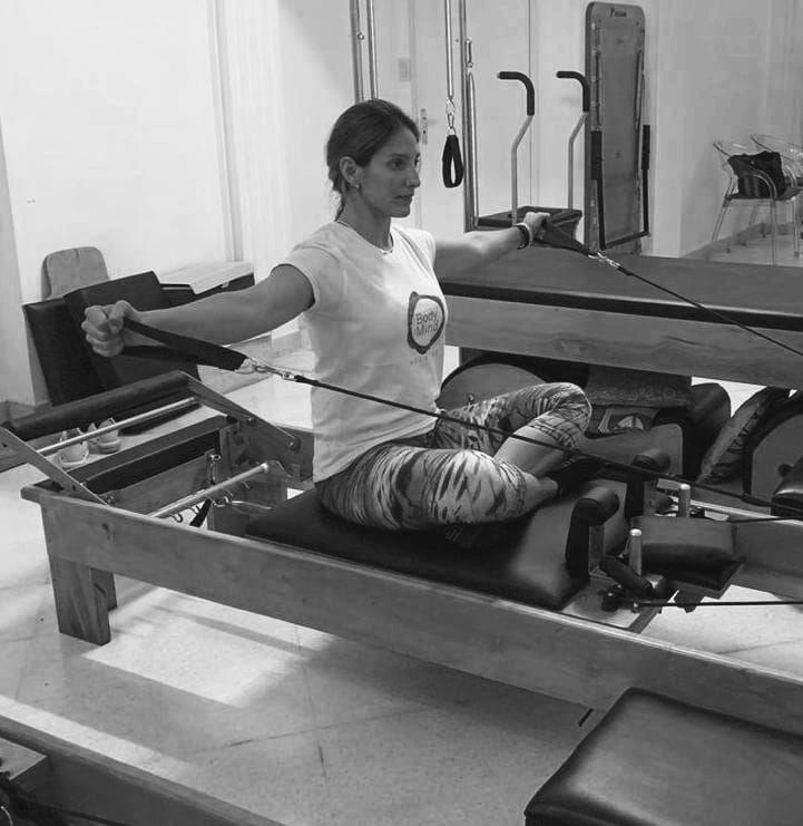 mujer realizando ejercicio de pilates reformer conocido como  escapular adduction