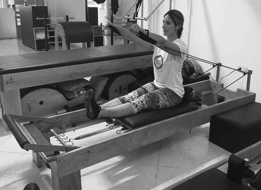 mujer realizando ejercicio de pilates reformer conocido como sitting rowing