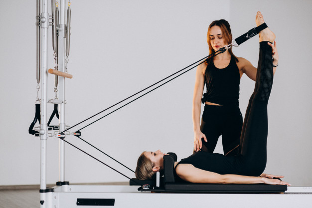 profesora de pilates realizando clase particular de reformer a su cliente